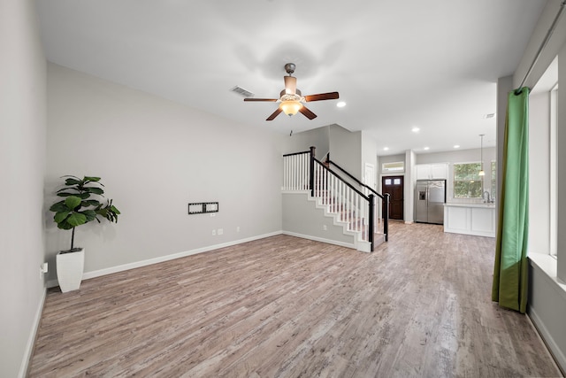 unfurnished living room with stairs, visible vents, a ceiling fan, and light wood-style floors