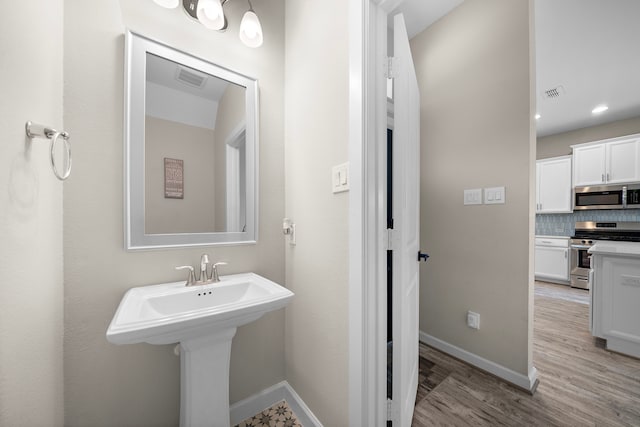 bathroom featuring wood finished floors, visible vents, tasteful backsplash, and baseboards