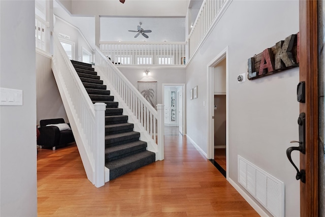 entryway featuring a high ceiling, ceiling fan, light wood finished floors, stairs, and visible vents