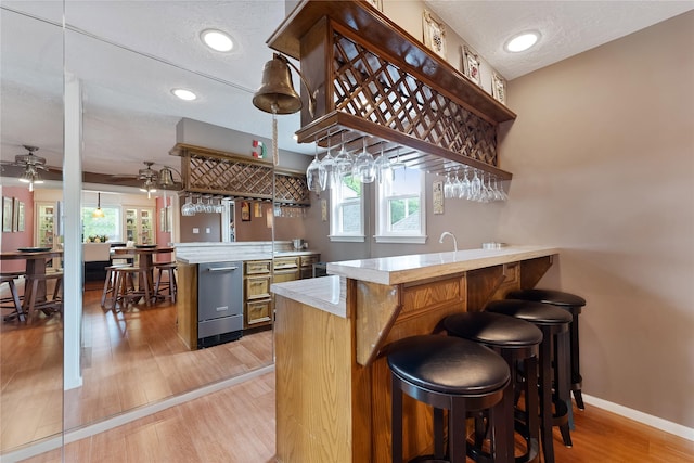 bar with indoor wet bar, a ceiling fan, plenty of natural light, and light wood-style floors