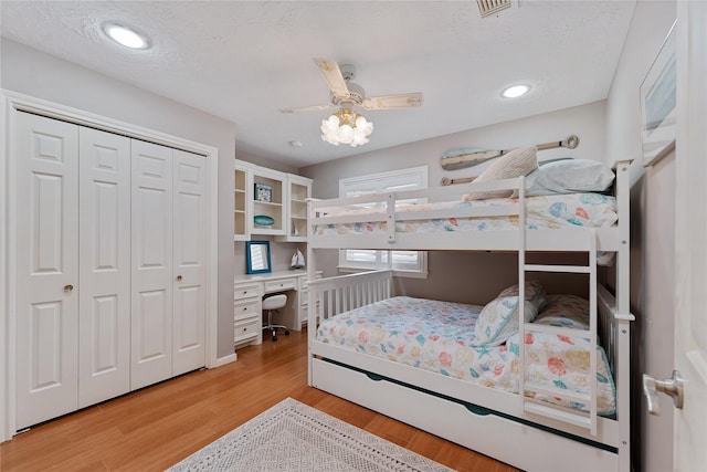 bedroom featuring built in study area, light wood-style floors, a ceiling fan, visible vents, and a closet