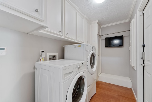 clothes washing area featuring a textured ceiling, washing machine and dryer, cabinet space, baseboards, and light wood-style floors