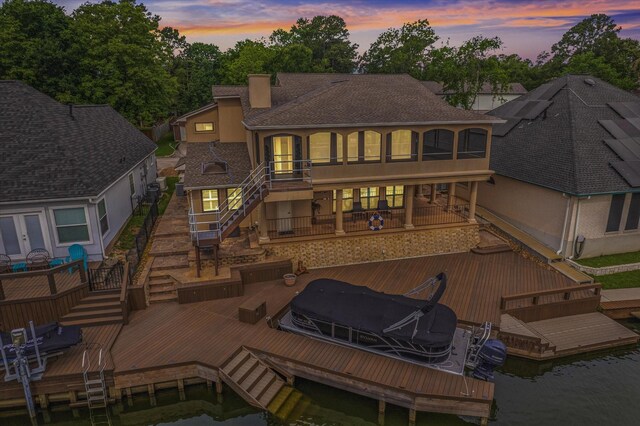 back of property featuring stairway, boat lift, a water view, and roof with shingles