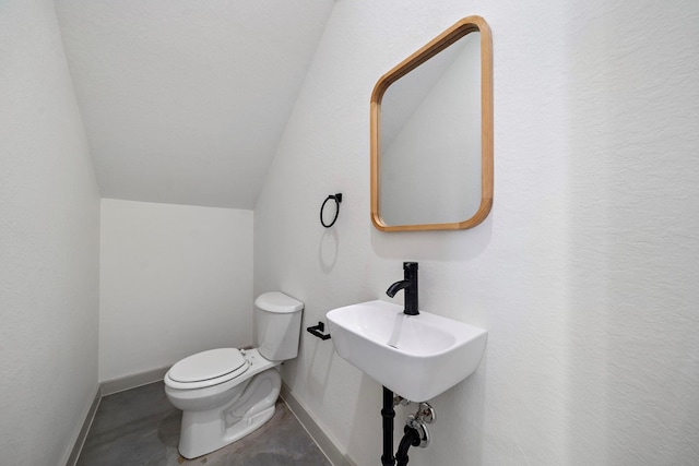 half bathroom with baseboards, toilet, and lofted ceiling