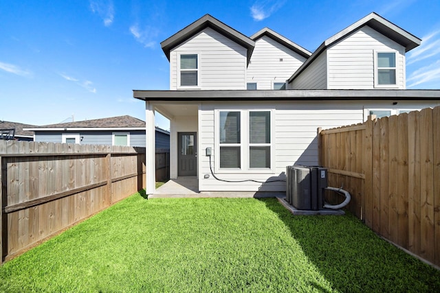 back of property with central AC, a fenced backyard, and a lawn