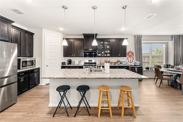 kitchen with a breakfast bar, stainless steel appliances, light wood-type flooring, a sink, and visible vents