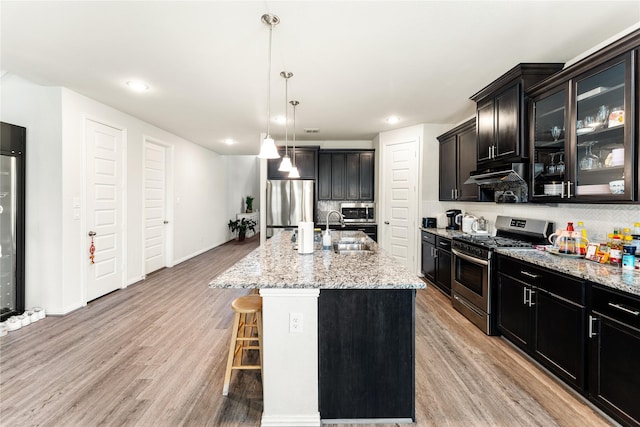 kitchen with light stone countertops, a sink, stainless steel appliances, decorative backsplash, and a breakfast bar area