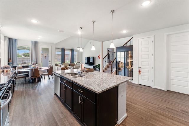 kitchen with light stone countertops, a sink, stainless steel appliances, wood finished floors, and open floor plan