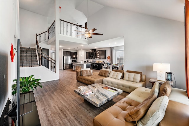 living room featuring a towering ceiling, a ceiling fan, stairway, and wood finished floors