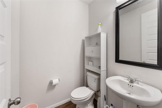 bathroom with a sink, toilet, visible vents, baseboards, and wood finished floors