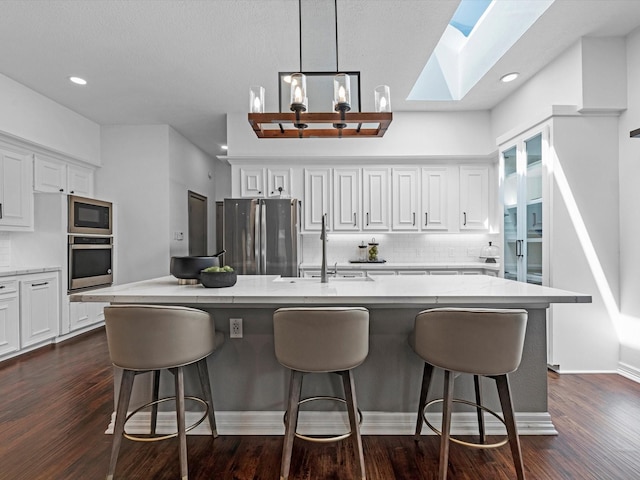 kitchen featuring decorative backsplash, white cabinetry, a sink, appliances with stainless steel finishes, and a skylight