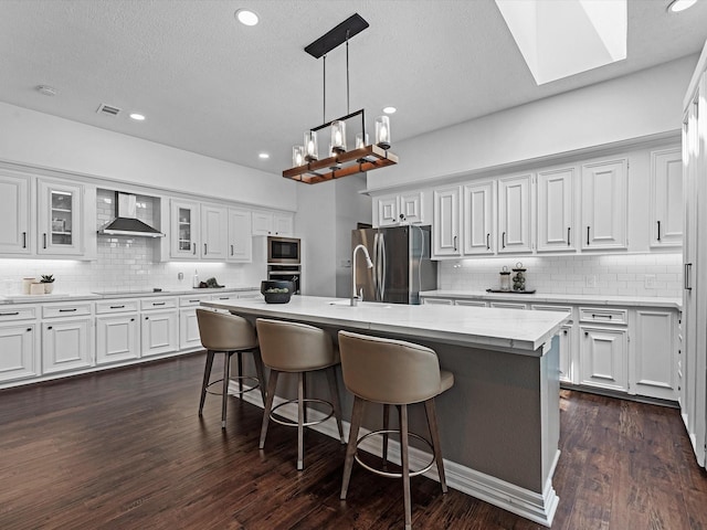 kitchen with a skylight, backsplash, stainless steel appliances, and wall chimney exhaust hood