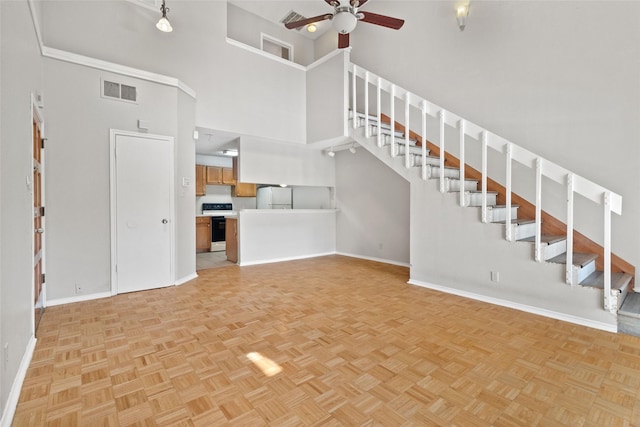 unfurnished living room with visible vents, ceiling fan, baseboards, stairway, and a high ceiling