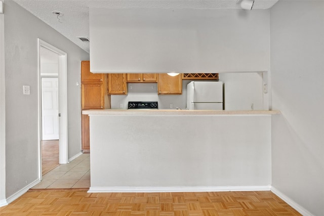 kitchen with brown cabinets, stove, freestanding refrigerator, and baseboards