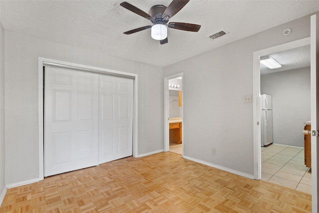 unfurnished bedroom featuring freestanding refrigerator, a closet, baseboards, visible vents, and a textured ceiling