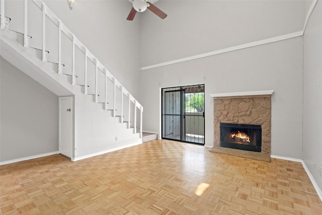 unfurnished living room featuring stairway, ceiling fan, baseboards, a fireplace, and a towering ceiling