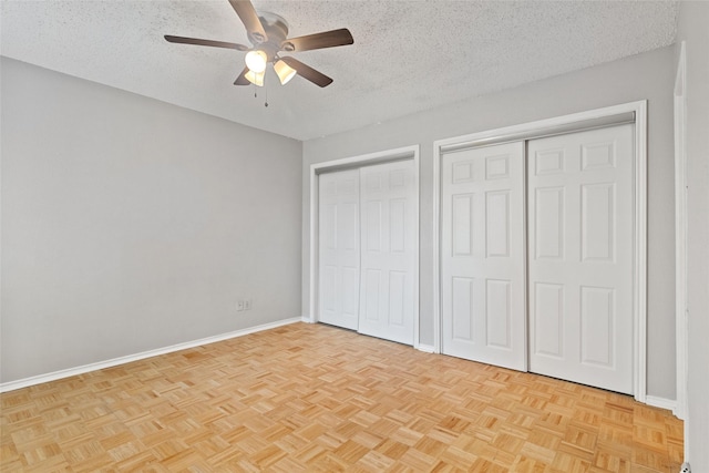 unfurnished bedroom with a textured ceiling, two closets, and baseboards
