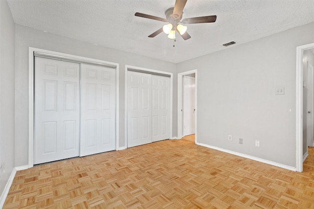 unfurnished bedroom with a textured ceiling, two closets, visible vents, and baseboards