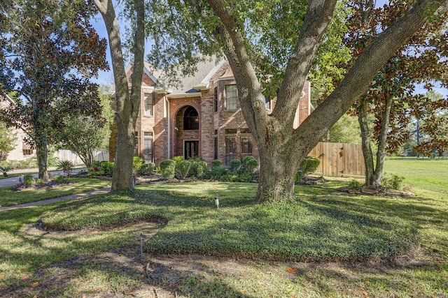 view of front of home featuring brick siding, fence, and a front lawn