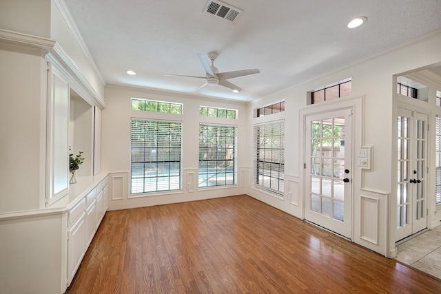 unfurnished sunroom featuring visible vents, wood finished floors, crown molding, and a decorative wall
