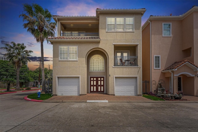 view of property with an attached garage, stucco siding, a balcony, and a tile roof