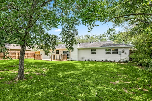 back of property with a deck, a yard, and fence