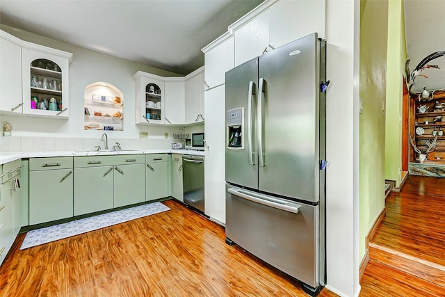 kitchen with stainless steel appliances, green cabinets, light wood-style flooring, and a sink