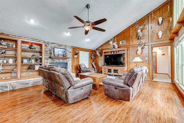 living room with ceiling fan, a stone fireplace, a wealth of natural light, and wood finished floors