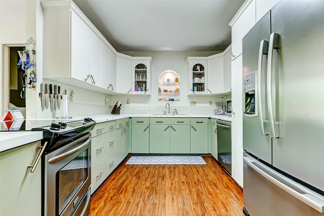 kitchen featuring light wood finished floors, a sink, green cabinets, light countertops, and appliances with stainless steel finishes