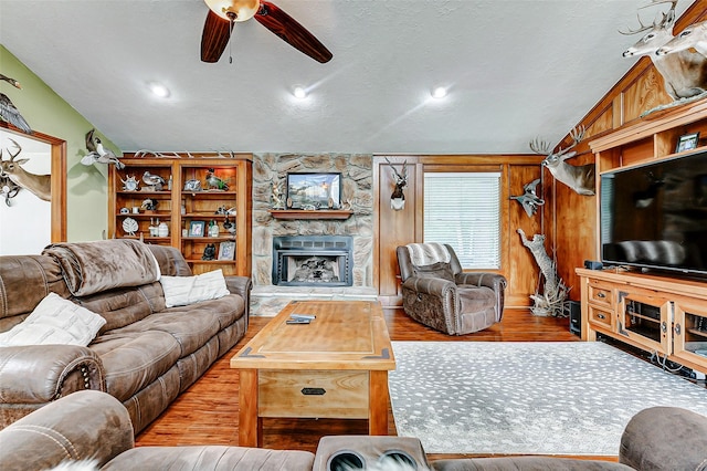 living room with wood finished floors, vaulted ceiling, a fireplace, a ceiling fan, and a textured ceiling