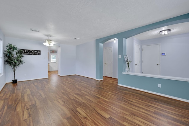 3739 Apple Hollow Ln, Humble, TX 77396 - unfurnished living room featuring dark wood-style flooring, a ceiling fan, arched walkways, a textured ceiling, and baseboards