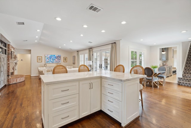 kitchen featuring light stone counters, a kitchen breakfast bar, white cabinetry, lofted ceiling, and visible vents