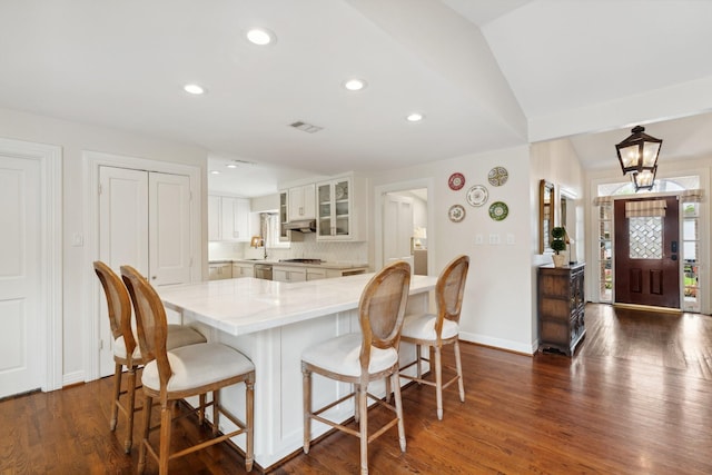 kitchen with dark wood finished floors, recessed lighting, white cabinetry, a kitchen bar, and glass insert cabinets