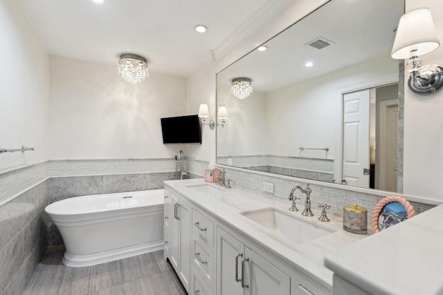 full bathroom featuring visible vents, double vanity, a freestanding tub, tile walls, and a sink