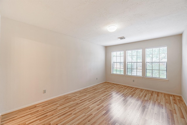 empty room with a textured ceiling, visible vents, light wood-style flooring, and baseboards
