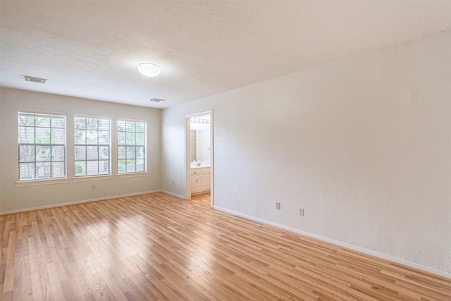 spare room featuring a textured ceiling, visible vents, light wood-type flooring, and baseboards