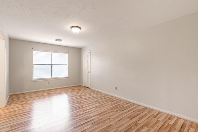 empty room with baseboards, visible vents, light wood-style floors, and a textured ceiling