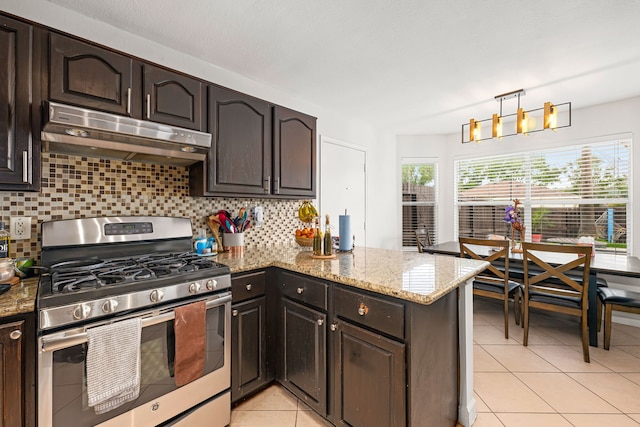 kitchen featuring a peninsula, stainless steel range with gas cooktop, under cabinet range hood, tasteful backsplash, and light tile patterned floors