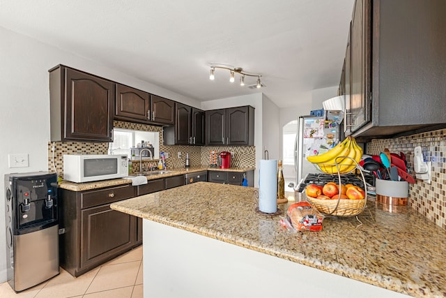 kitchen with dark brown cabinets, a sink, white microwave, freestanding refrigerator, and a peninsula