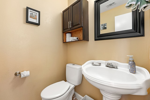 half bathroom featuring toilet, visible vents, and a sink