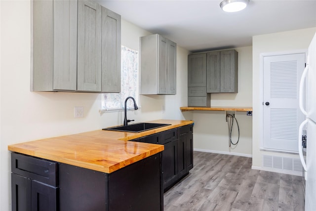 kitchen featuring wood counters, light wood-style flooring, a sink, freestanding refrigerator, and baseboards
