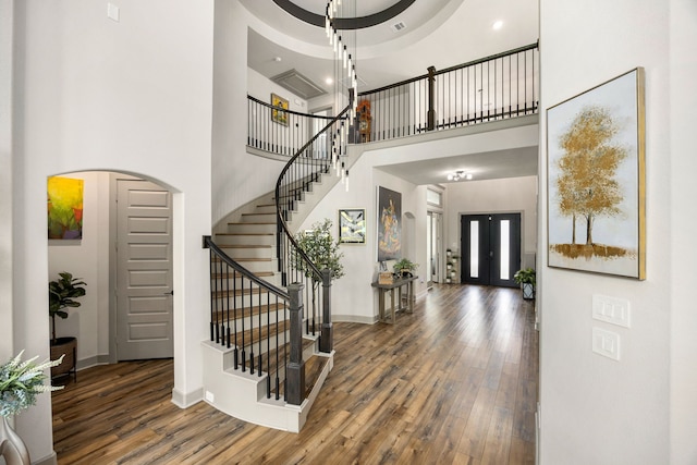 entryway with arched walkways, stairs, baseboards, wood finished floors, and a towering ceiling