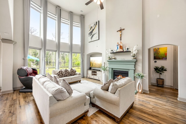 living area featuring a glass covered fireplace, a high ceiling, hardwood / wood-style flooring, and ceiling fan