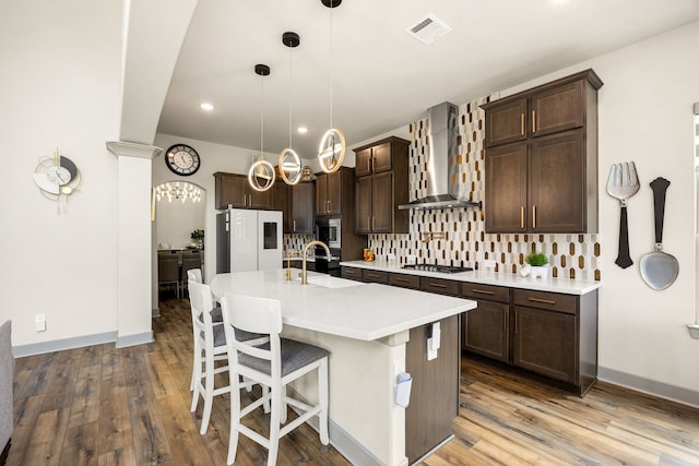 kitchen featuring visible vents, tasteful backsplash, a sink, stainless steel appliances, and wall chimney exhaust hood