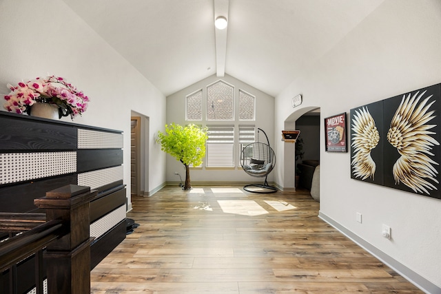 interior space featuring arched walkways, baseboards, lofted ceiling with beams, and light wood-style floors