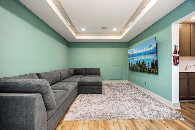 living room with visible vents, wood finished floors, baseboards, a tray ceiling, and recessed lighting