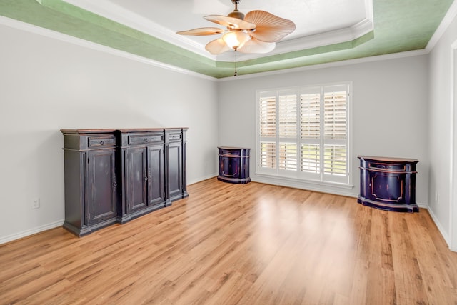 empty room with ceiling fan, light wood-type flooring, crown molding, and a tray ceiling