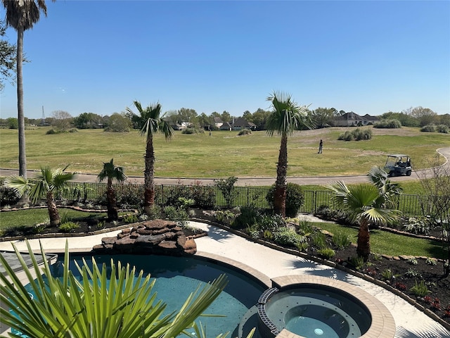 view of swimming pool featuring fence, a lawn, and a pool with connected hot tub