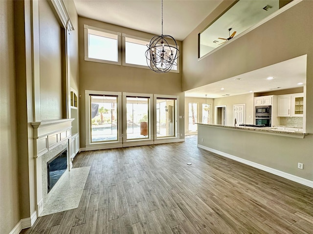 unfurnished living room featuring wood finished floors, a notable chandelier, a premium fireplace, and baseboards
