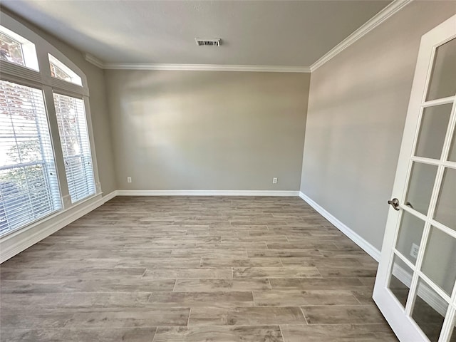 empty room with wood finished floors, visible vents, ornamental molding, and baseboards